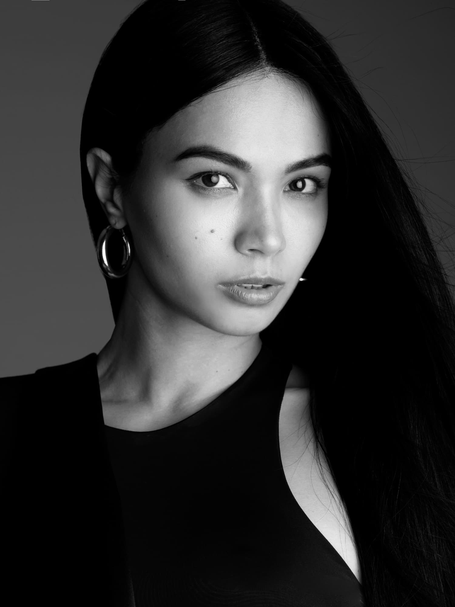 Black-and-white close-up of Shirin Hojayeva in hoop earrings and a black top, gazing directly with quiet intensity.