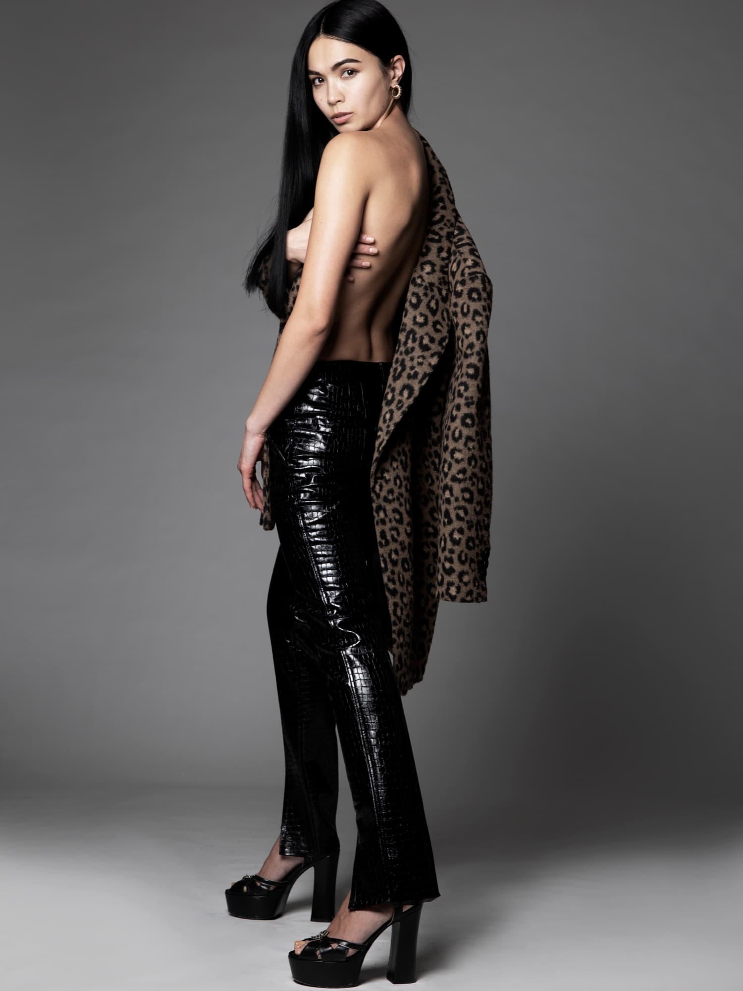 Shirin Hojayeva glances over her shoulder in a leopard-print coat and black vinyl pants against a gray studio backdrop.
