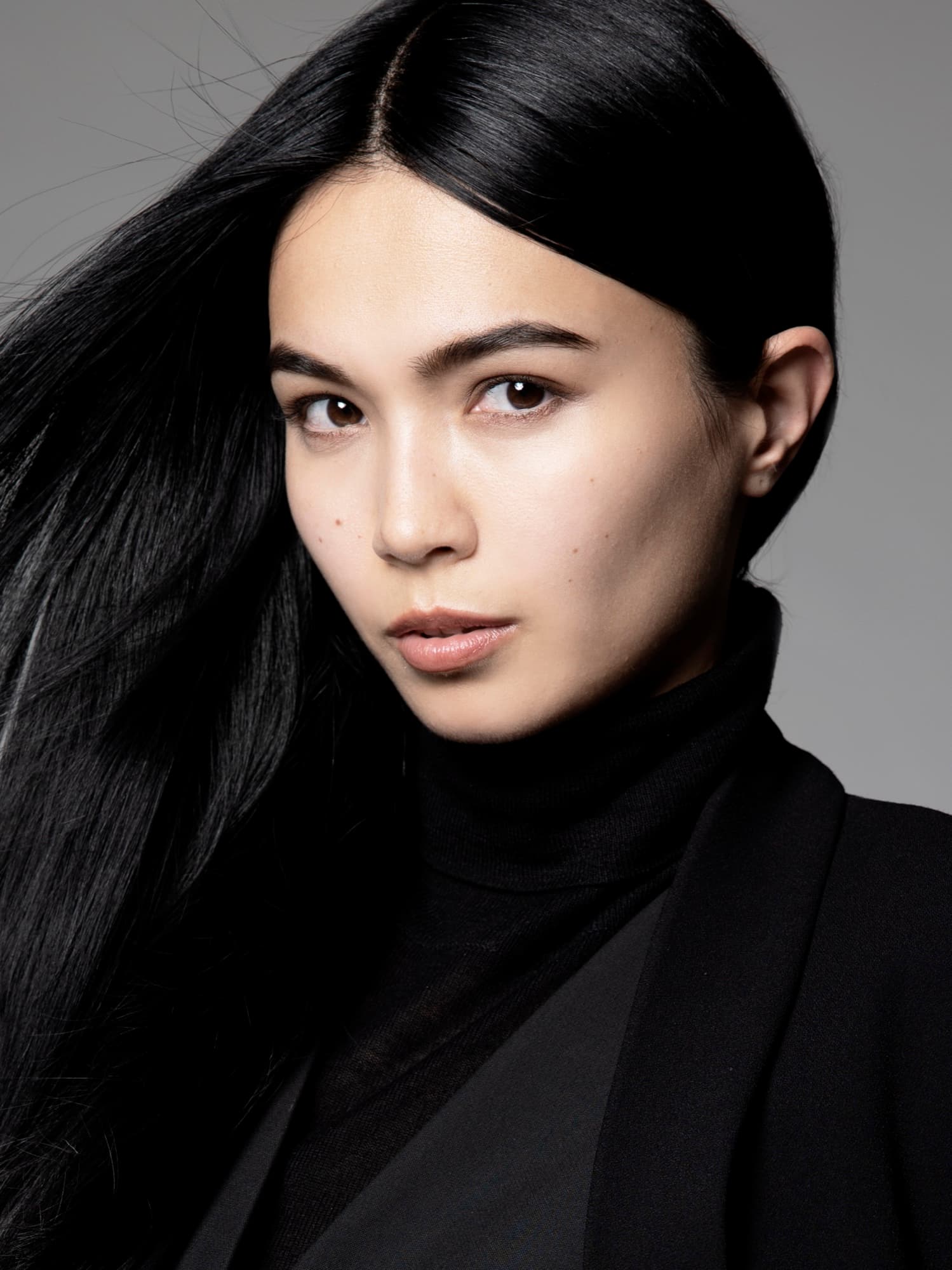 Close-up of Shirin Hojayeva in a black turtleneck and blazer, hair flowing, with a calm and focused expression.