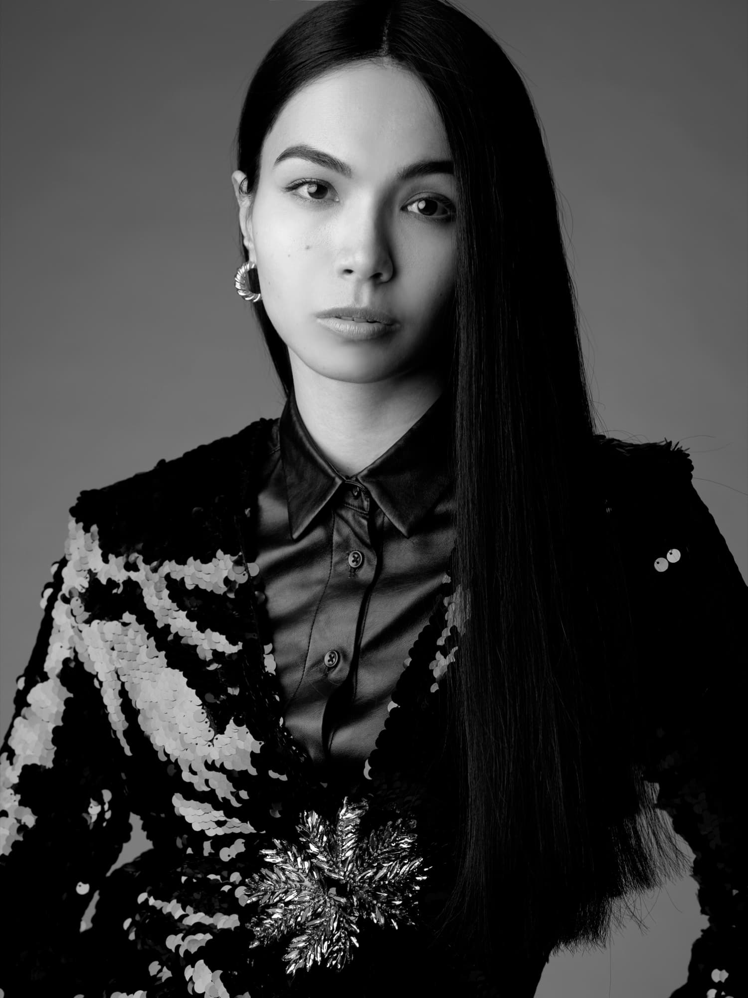 Black-and-white portrait of Shirin Hojayeva in a sequined blazer and satin shirt with a stern, editorial expression.