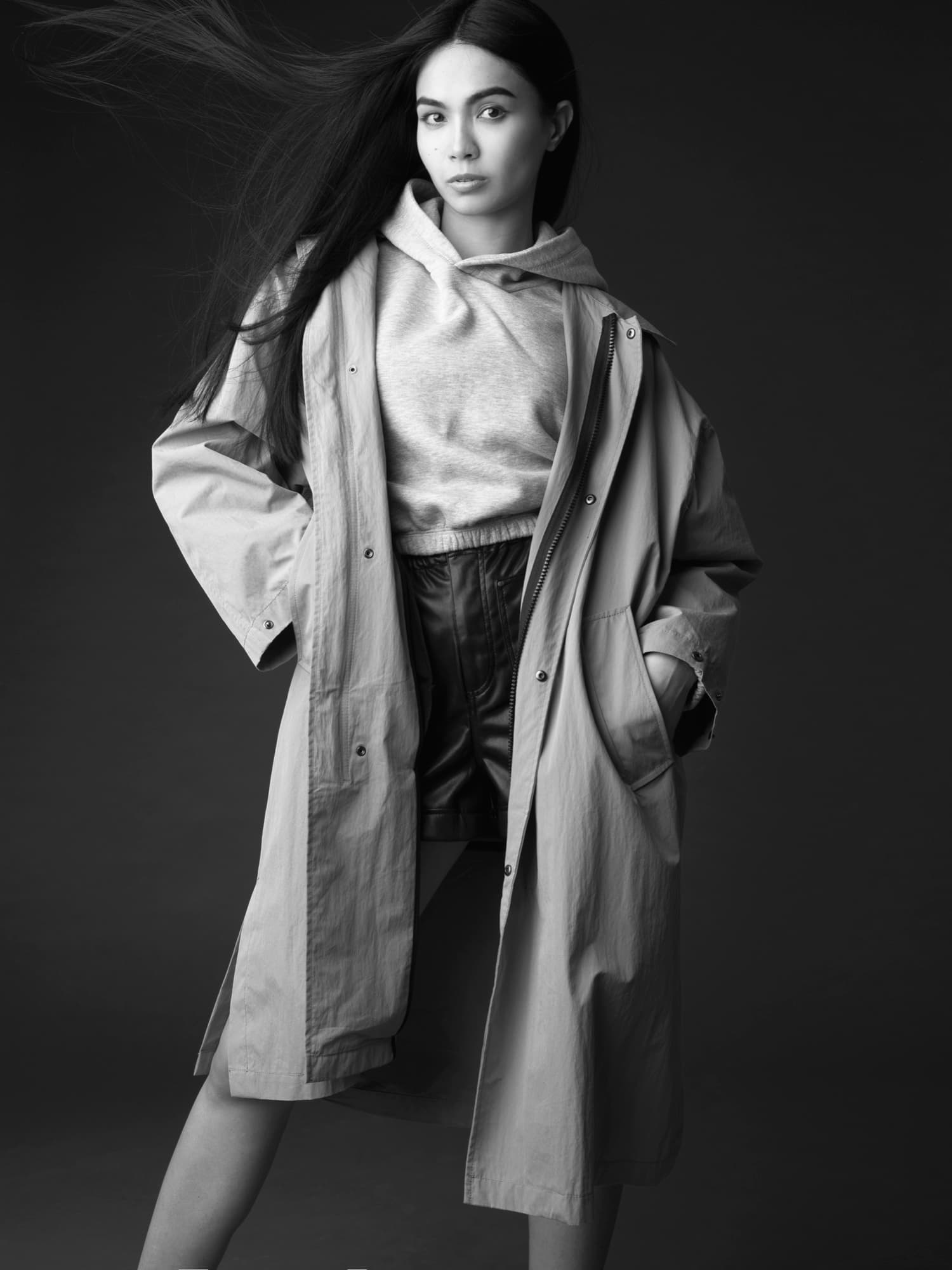 Black-and-white studio shot of Shirin Hojayeva in an oversized parka and hoodie with windblown hair, looking effortless.