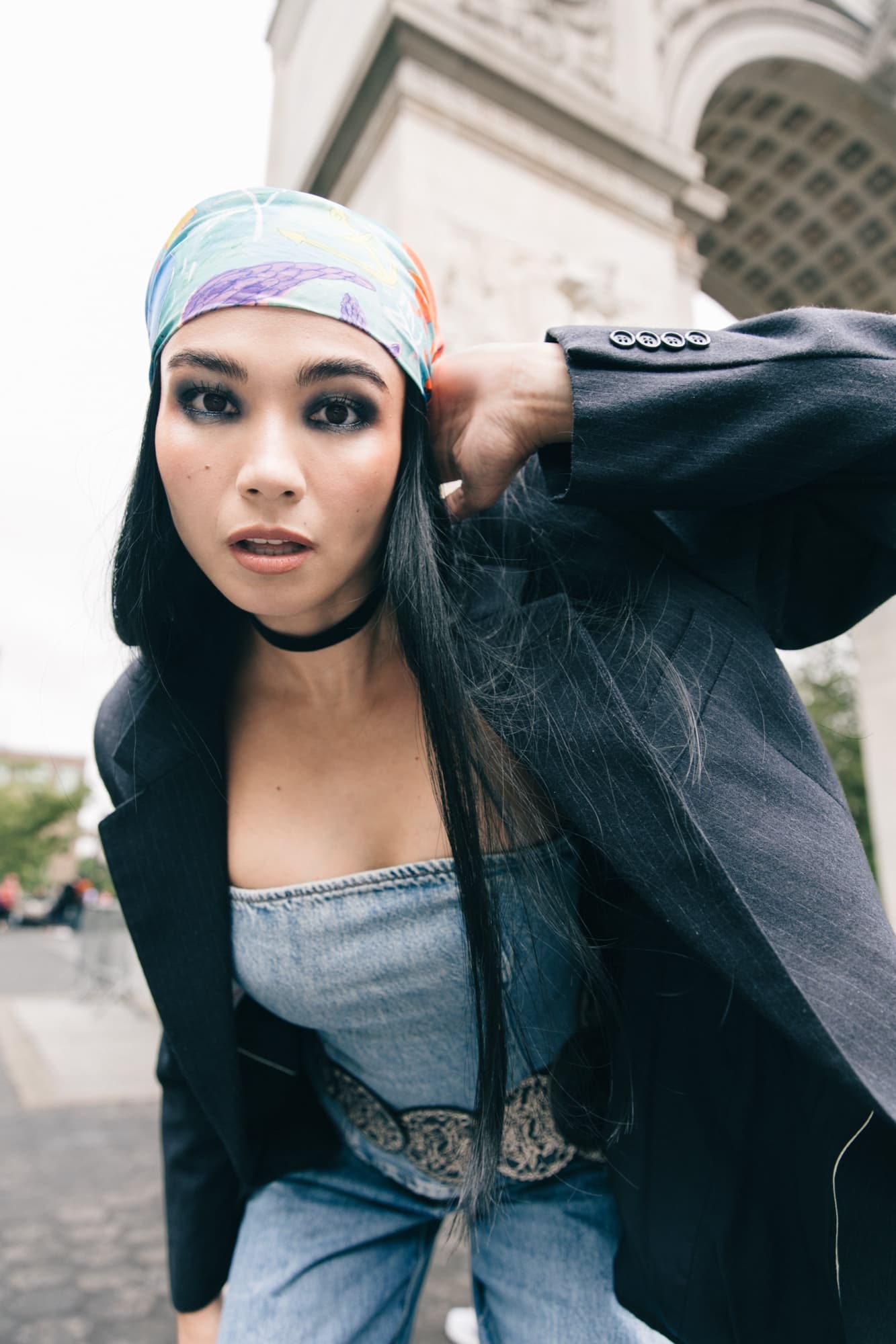 Shirin Hojayeva poses near Washington Square Arch in a blazer, denim top, and headscarf with bold smoky-eye makeup.