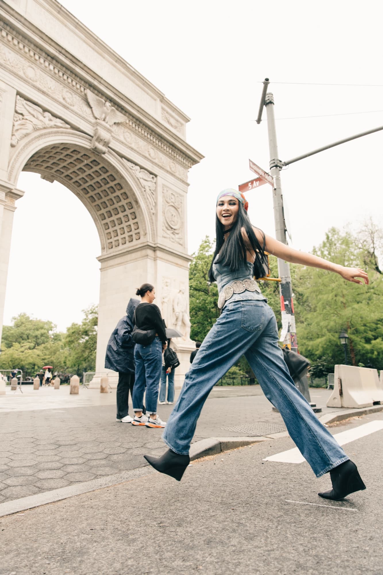 Shirin strides joyfully past the Washington Square Arch in a denim outfit and headscarf, radiating carefree energy.