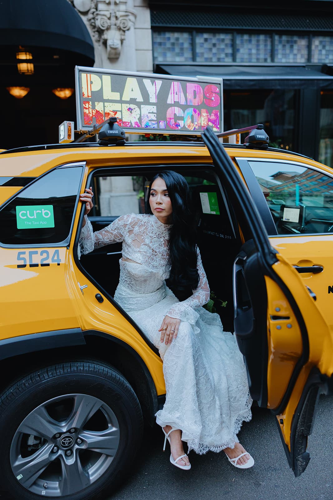 Shirin steps out of a yellow NYC taxi in a white lace gown and heeled sandals, exuding effortless glamour.