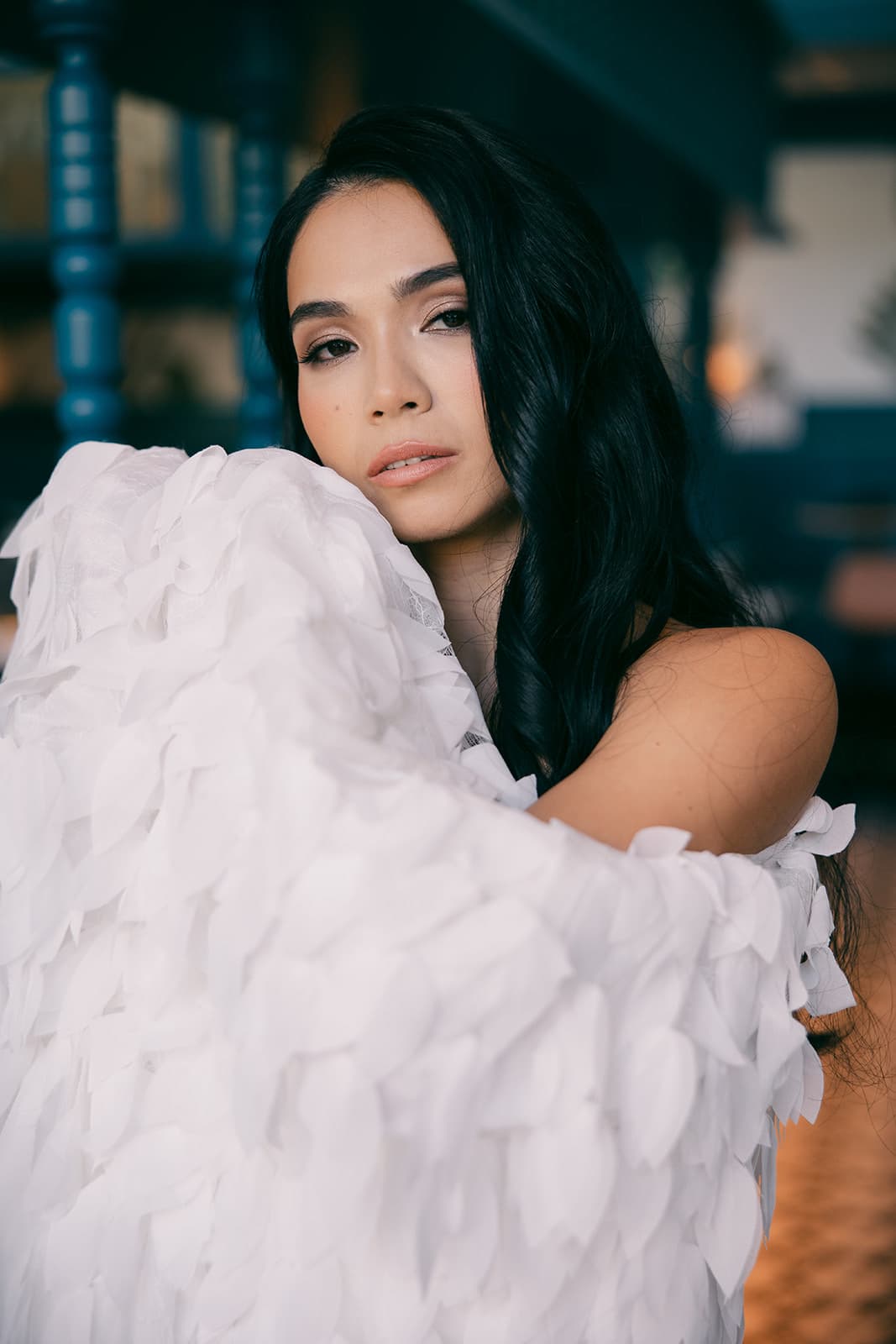 Close-up of Shirin wrapped in a white petal-textured garment, gazing softly at the camera with warm toned light.