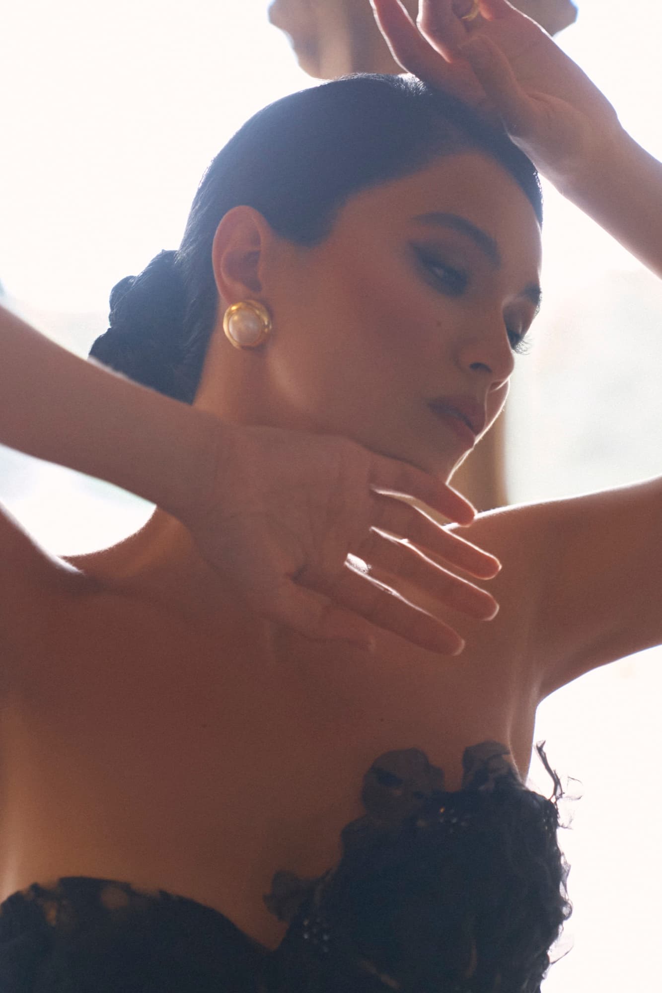 Shirin tilts her head with eyes closed, gold earring catching the light, in an artistic warm-toned close-up.