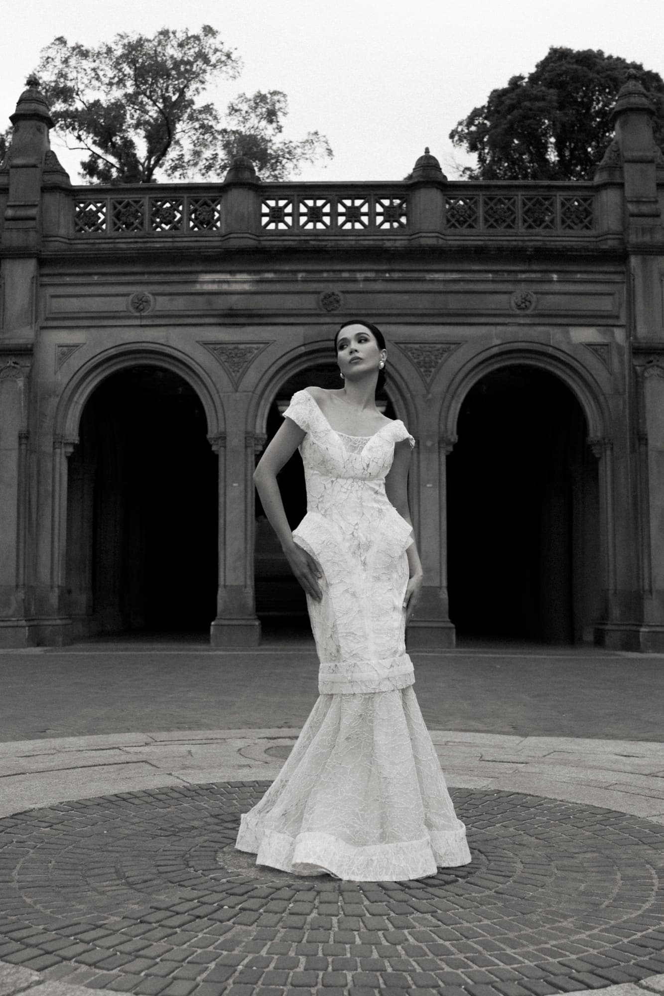 Black-and-white full-length shot of Shirin in a white lace mermaid gown before the Bethesda Terrace arches.