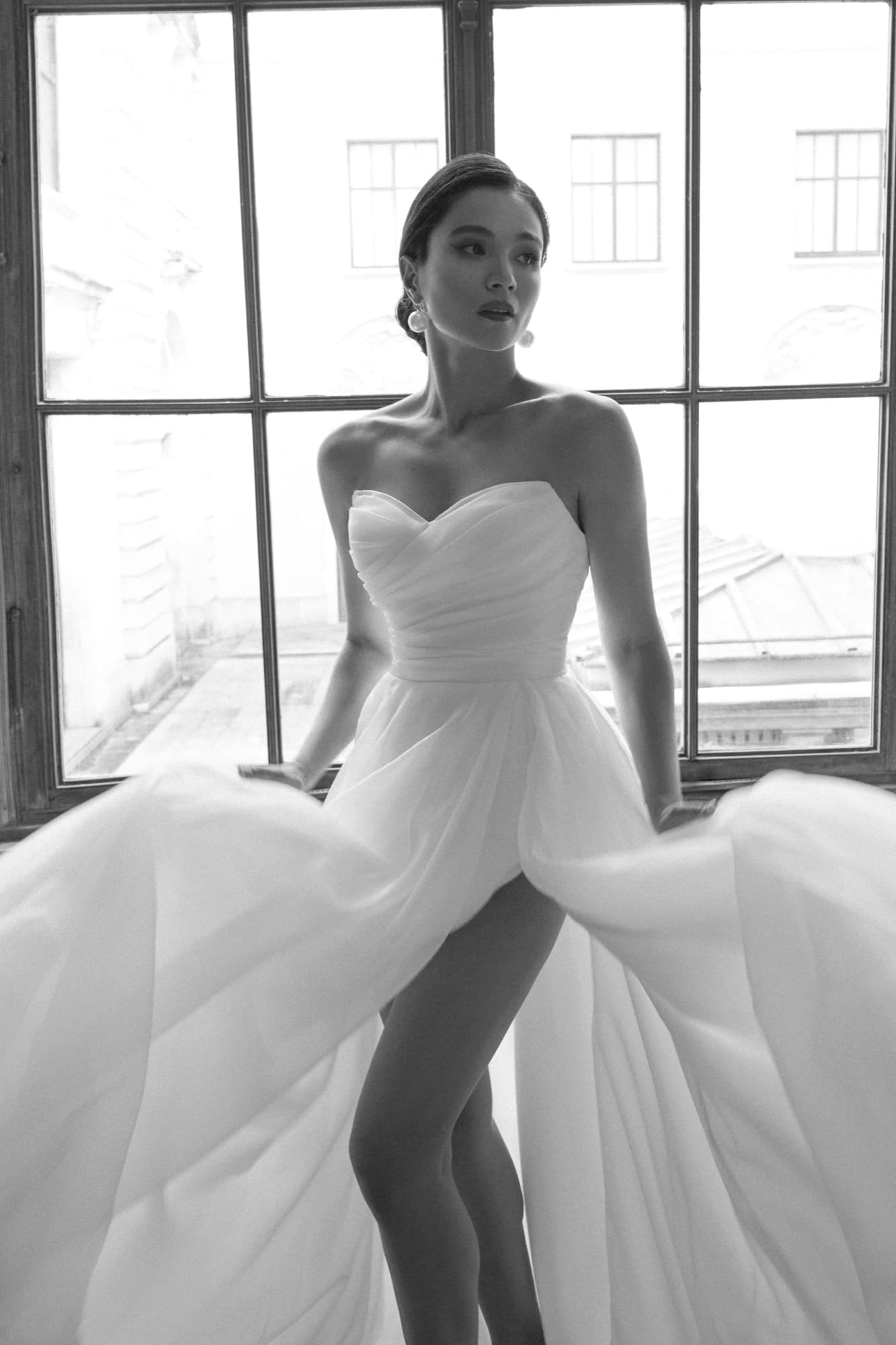 Black-and-white shot of Shirin seated on a windowsill in a sweetheart tulle gown with a dramatic flowing skirt.