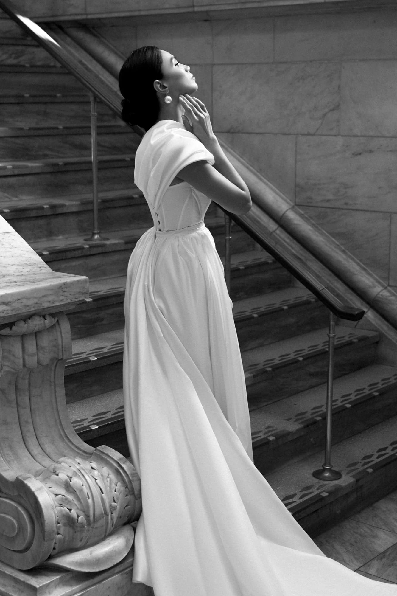 Black-and-white portrait of Shirin on marble stairs in a satin gown, head tilted back with hands at her neck.