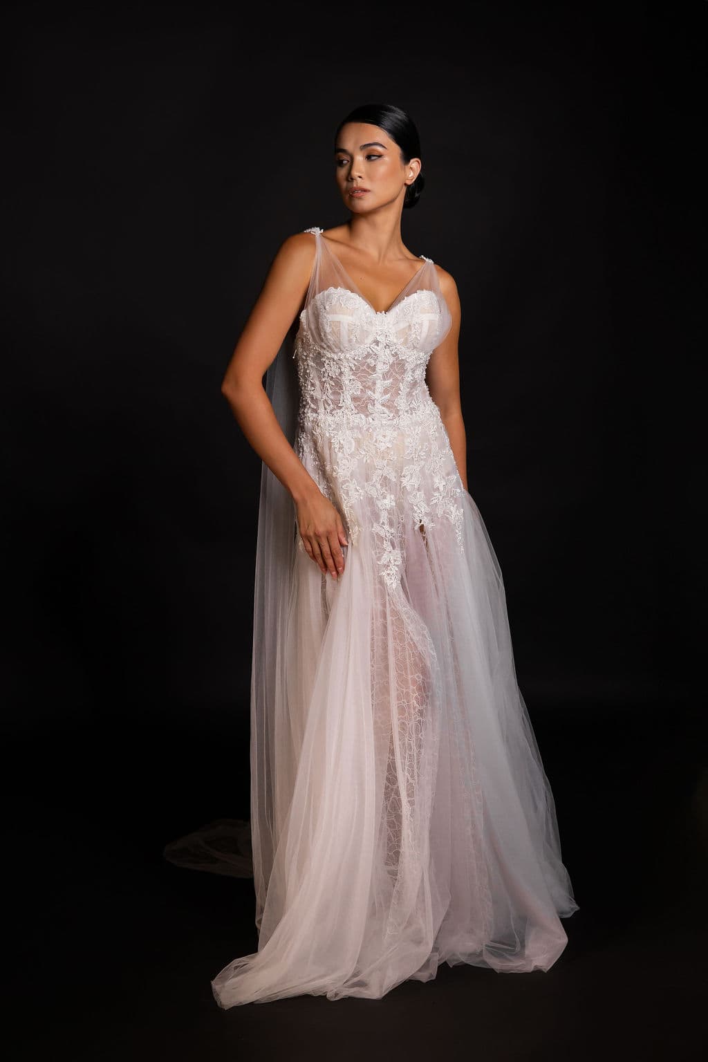 Shirin Hojayeva gazes softly aside in a white lace and tulle bridal gown with sheer overlay against a dark backdrop.