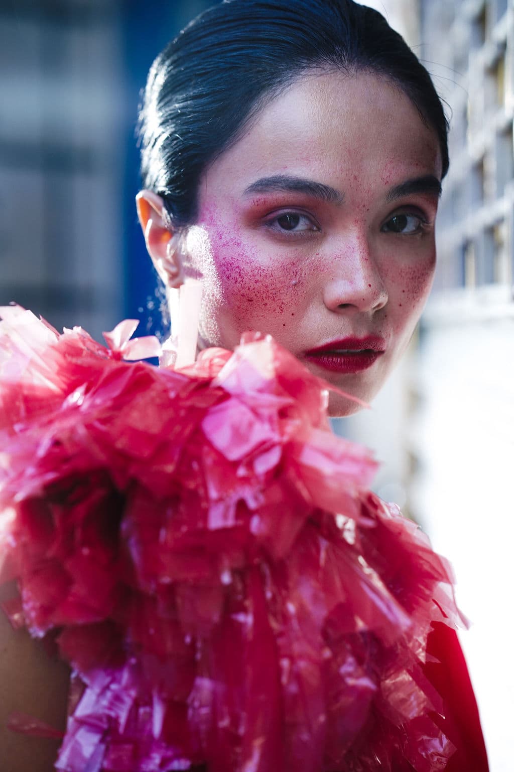Close-up of Shirin Hojayeva with pink glitter makeup and a ruffled pink cellophane collar, staring directly into camera.