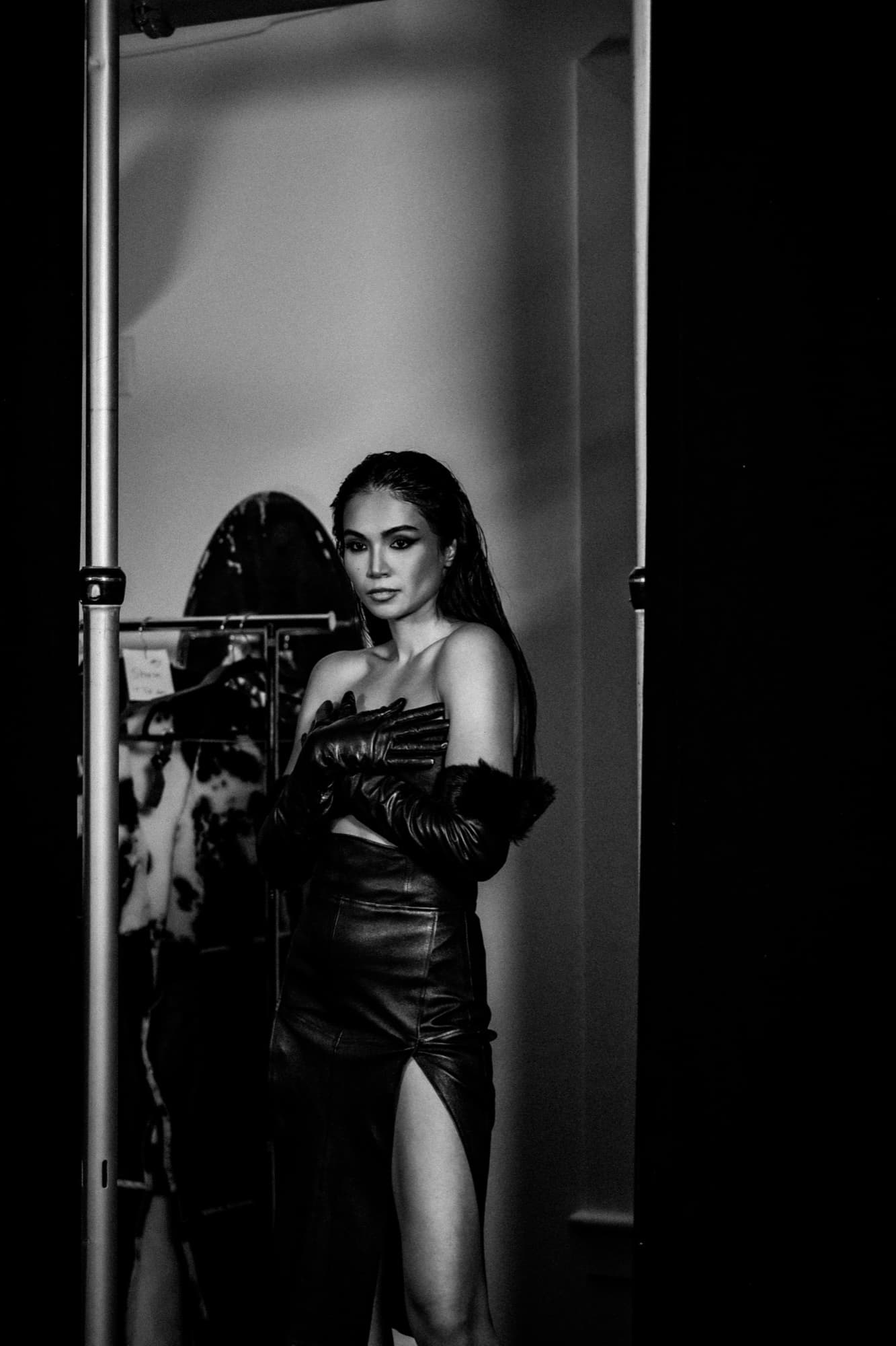 Black-and-white shot of Shirin Hojayeva framed in a doorway wearing a leather dress and gloves, backstage before a show.