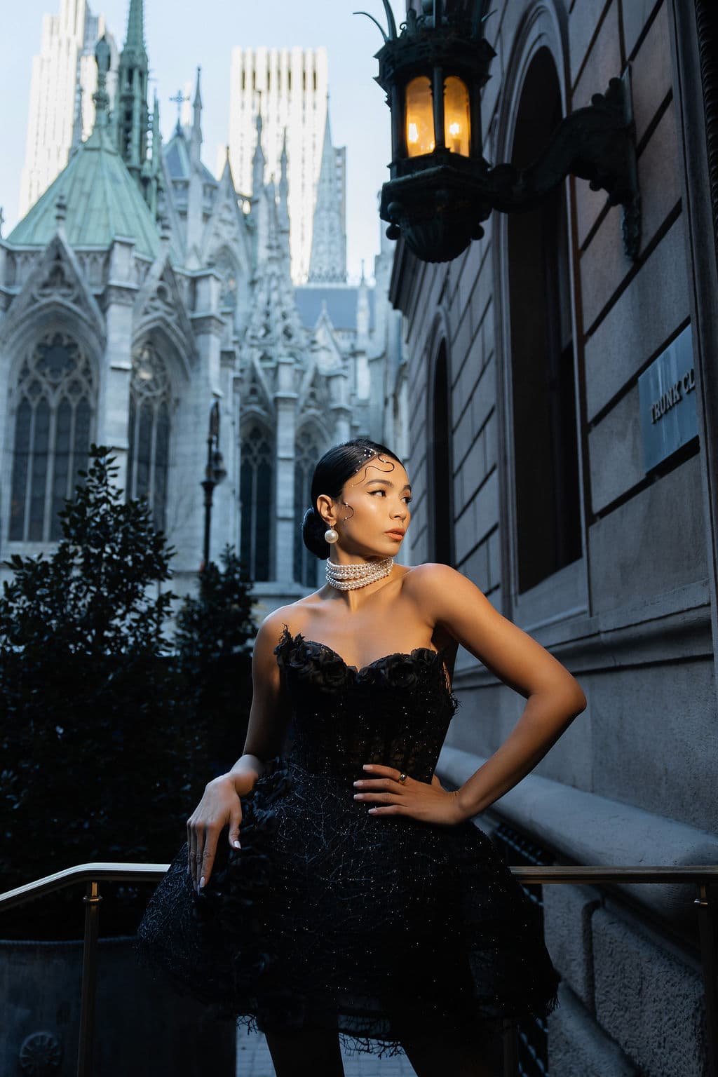Shirin Hojayeva poses at dusk in a black feathered corset gown with pearl choker near St. Patrick's Cathedral in NYC.